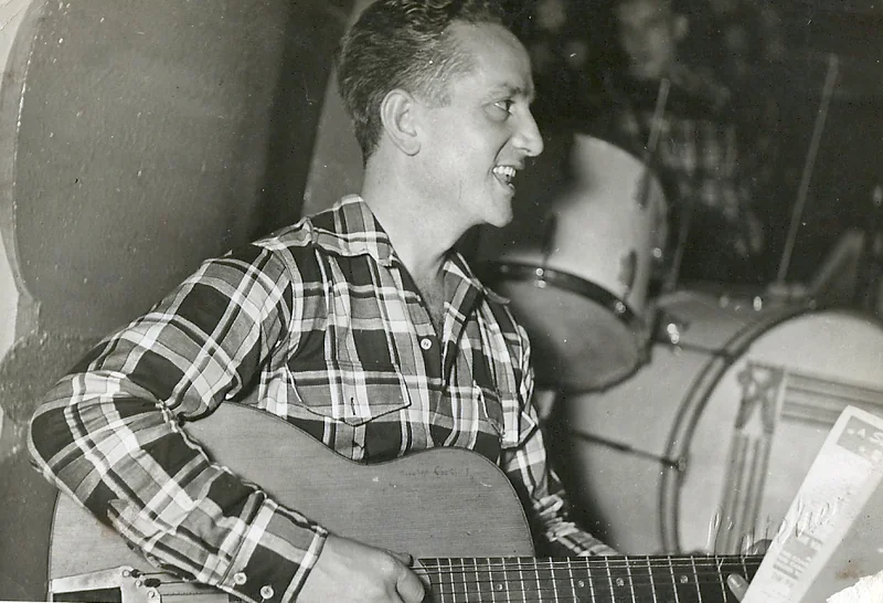 Con la chitarra, camicia a quadri, davanti alla batteria dell'orchestra.
